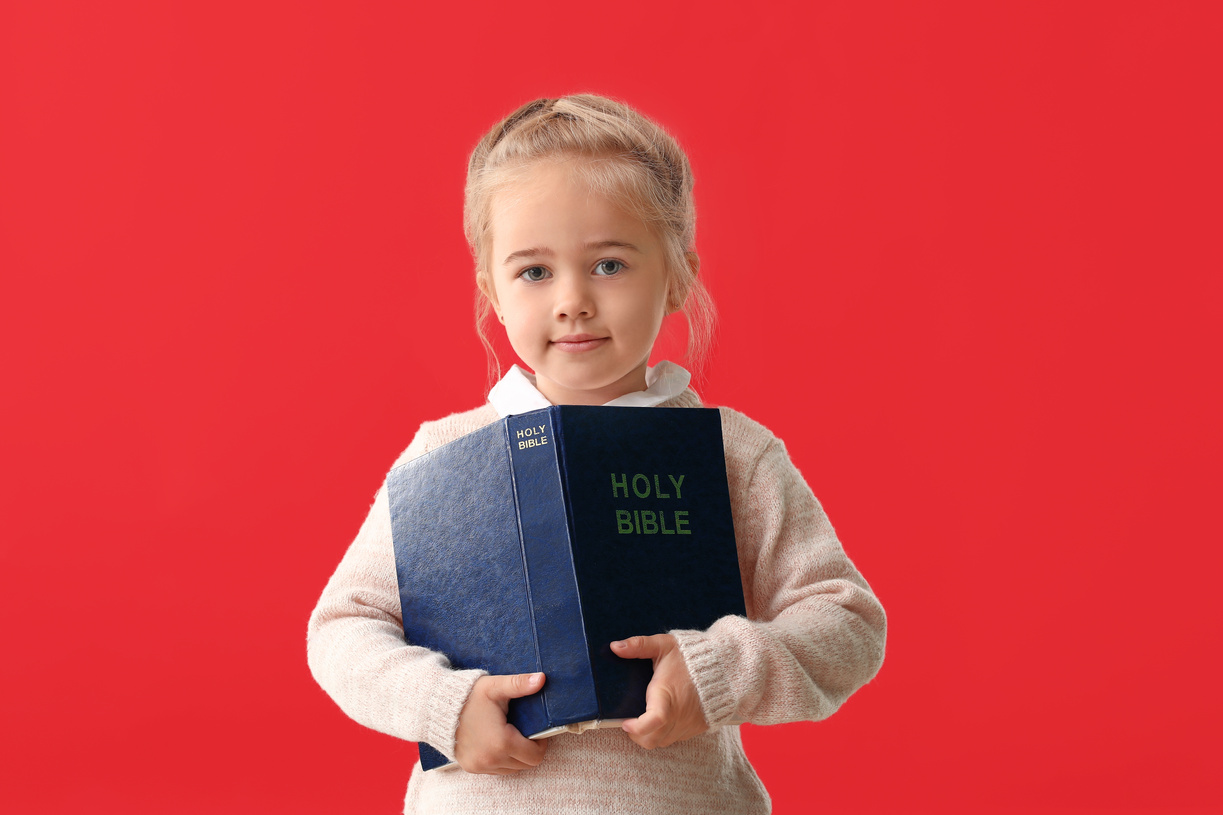 Little Girl with Bible on Color Red Background